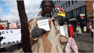 Manifestant africain contre le racisme anti-noir qui brandit 2 livres, Racisme anti-noir du CERAN et Code Noir le Calvaire de Canaan de Louis Sala-Molins (France, Belgique, Pays-Bas)