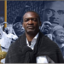 Acteur metteur en scène Peter Lema devant une affiche militante africaine pour les réparations