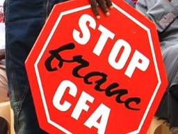Plan rapproché sur pancarte octogonale au texte blanc et noir sur fond rouge tenu par un manifestant africain anti-FCFA
